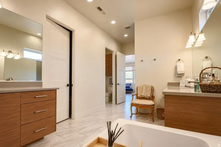 Dual wood-finish vanities with light-toned countertops, recessed lighting, and a built-in bathtub