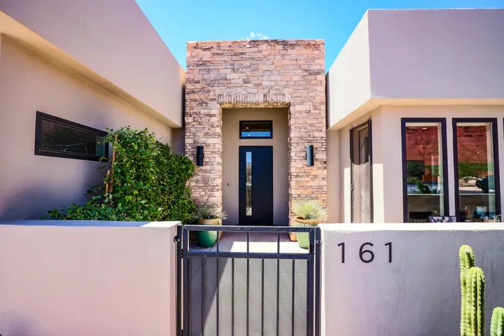 Stucco exterior with stone veneer accents, modern black entry door, and dark-framed windows