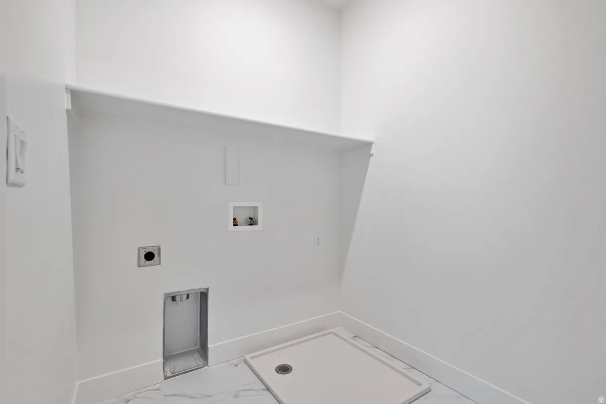 Dedicated laundry space featuring a utility sink pan, washer and dryer hookups, overhead shelving, and white baseboards