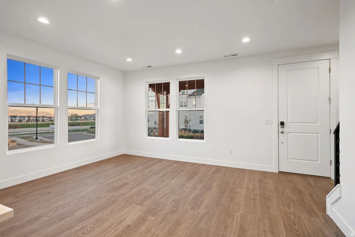 Spacious room featuring wood-finish flooring, white walls, and recessed lighting
