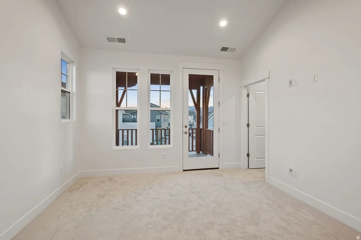 Room with neutral carpeting, recessed lighting, white walls, and a glass-paneled door leading to an exterior balcony