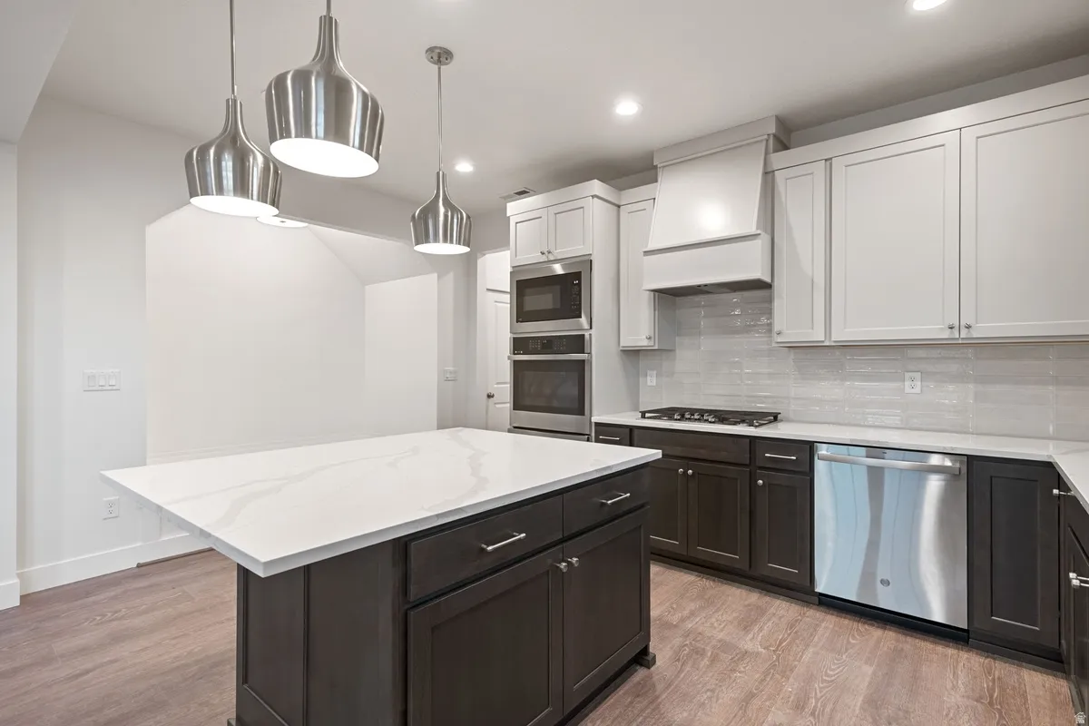 Kitchen featuring an expansive center island with a stone-finish countertop, stainless steel appliances, two-tone cabinetry, a tile backsplash, and wood-finish flooring