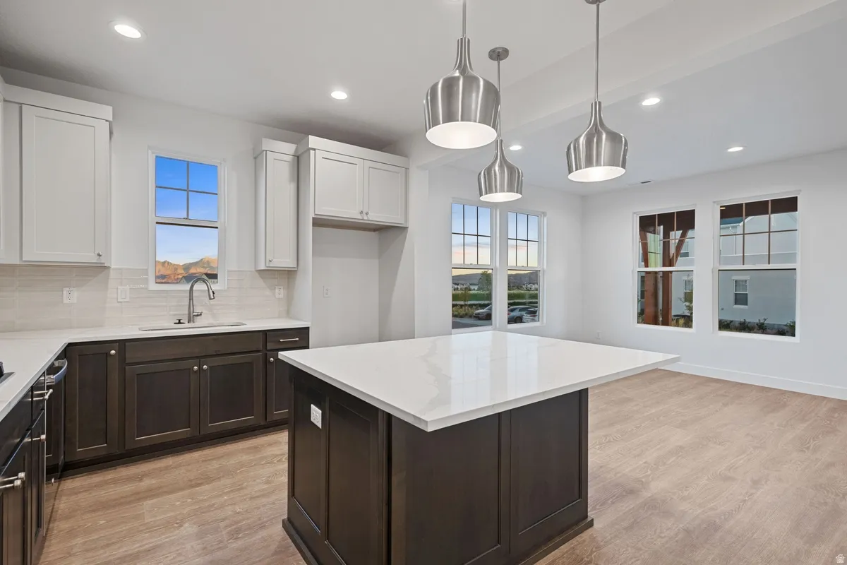 Kitchen featuring an island with a white countertop, dark wood-finish cabinetry, and stainless steel pendant lighting