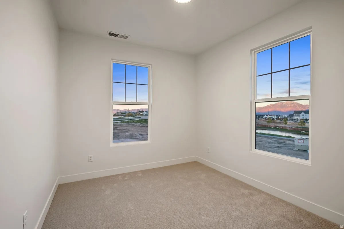Bright interior space featuring two large windows, white trim, light-colored carpeting, and a flush-mount ceiling light