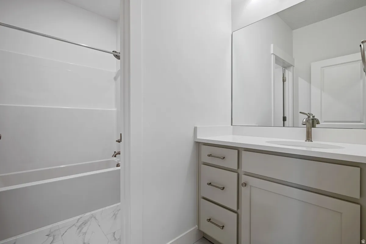 Bathroom featuring a single vanity with a white countertop, undermount sink, brushed nickel faucet, and light gray cabinetry with brushed nickel hardware