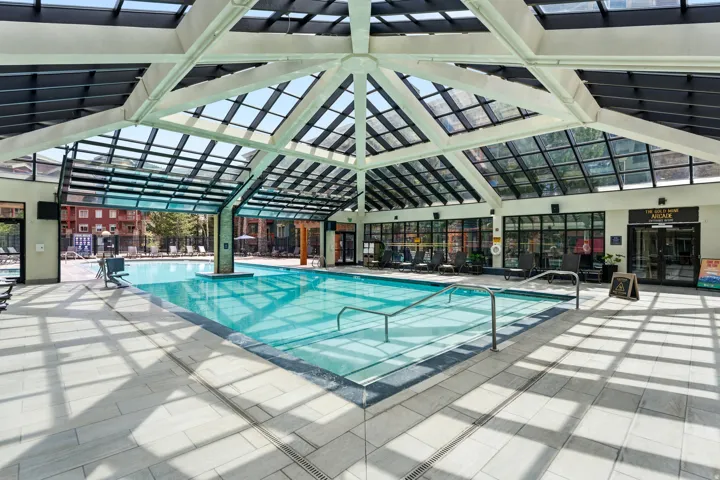 Indoor-outdoor aquatic facility featuring a large swimming pool, expansive glass ceiling, perimeter windows, and light-toned tile flooring