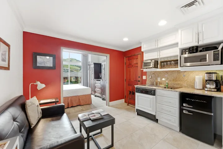 Compact kitchen area featuring white cabinetry, a stone countertop with a matching backsplash, and integrated appliances including a dishwasher and compact refrigerator