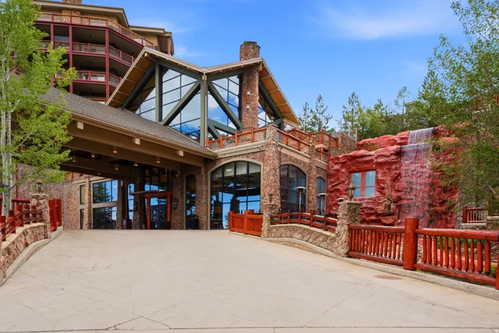 Grand entrance featuring a porte-cochère, stone facade, multi-story glass curtain wall, integrated water feature, and rustic log railings