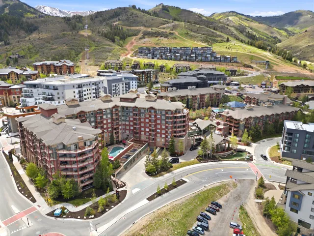 Multi-story development featuring a red brick and wood-paneled exterior, multiple private balconies, a central outdoor swimming pool, and landscaping with mature trees and shrubbery