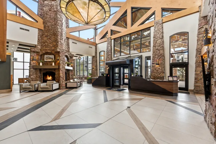 Grand entry with a stone fireplace, exposed timber beams, and a large central chandelier