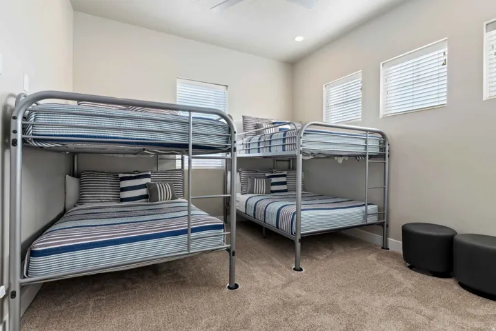 Carpeted room featuring two bunk beds with metal frames, multiple windows with blinds, and a ceiling fan