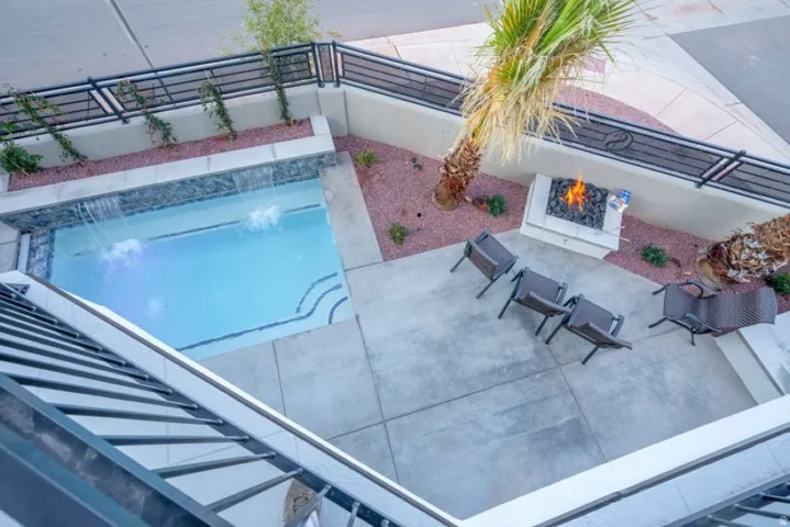 Outdoor patio featuring a rectangular swimming pool with waterfall features, a built-in fire pit, and concrete hardscaping