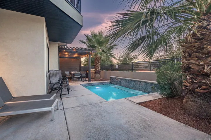 Concrete patio featuring a compact swimming pool with stone-clad waterfall and integrated spa