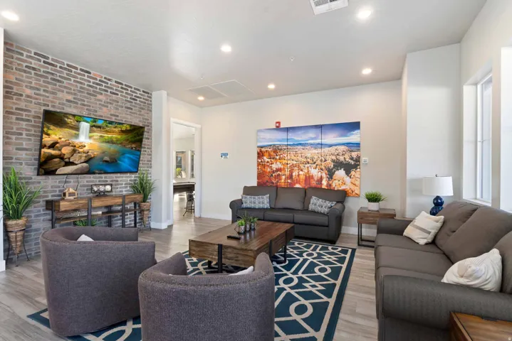 Spacious living area featuring a prominent exposed brick accent wall, recessed lighting, wood-finish flooring, and multiple windows for natural illumination
