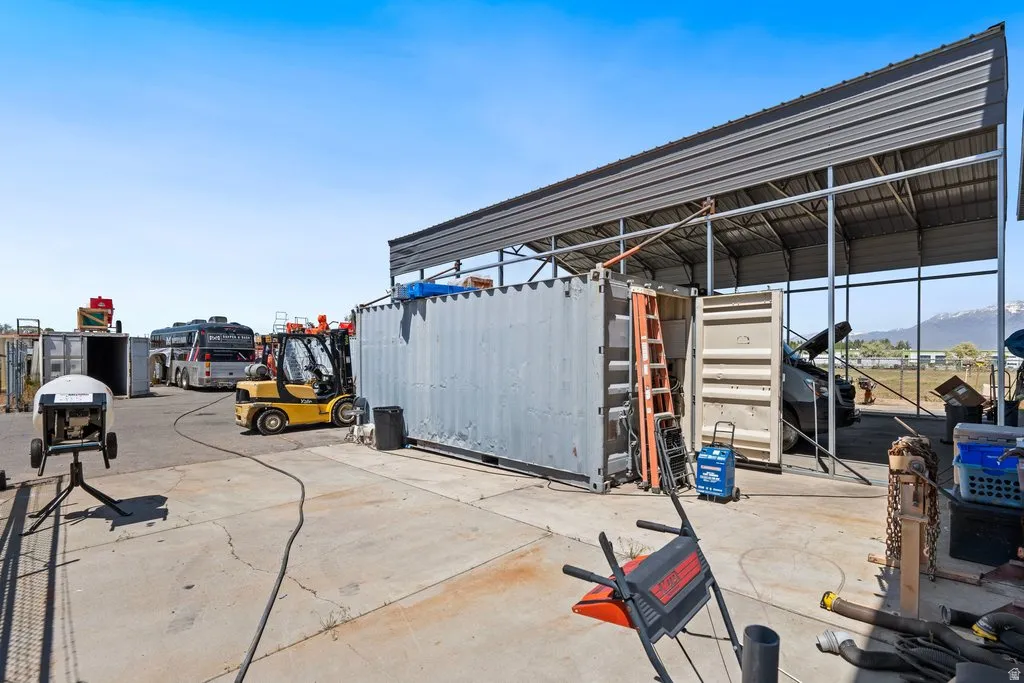 Expansive concrete lot featuring a large metal carport structure and multiple storage containers