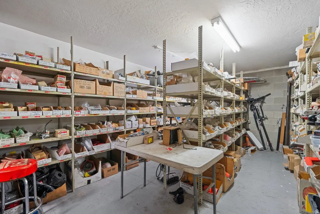 Utility room featuring extensive metal shelving, a work table, concrete block wall, and fluorescent lighting