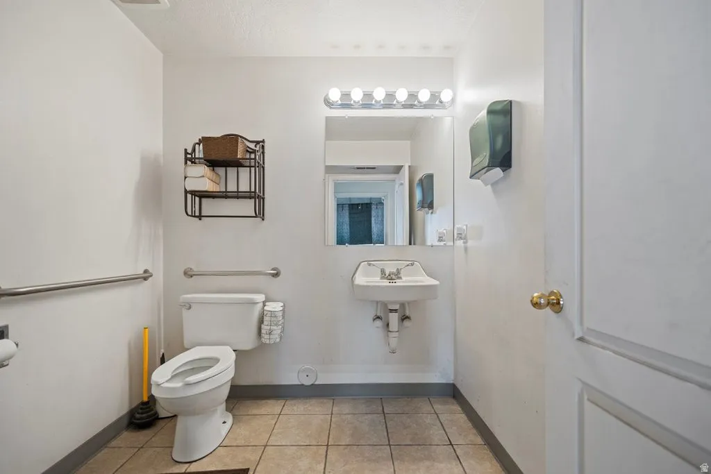 Powder room featuring a wall-mounted sink, ceramic tile flooring, and multiple grab bars