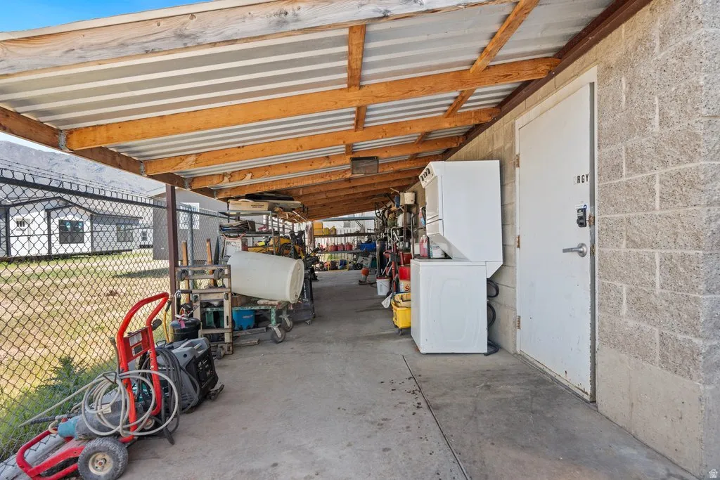 Covered outdoor area featuring a concrete floor, cinder block wall, and corrugated metal roof supported by wood beams