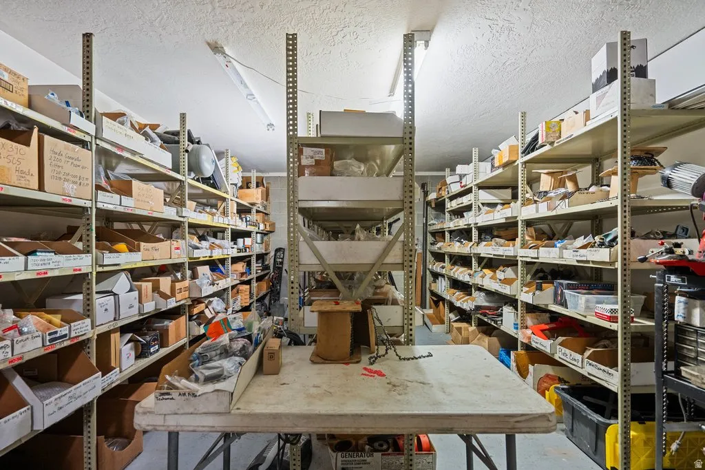 Spacious storage area featuring multiple rows of industrial metal shelving, fluorescent ceiling lights, and a textured ceiling finish