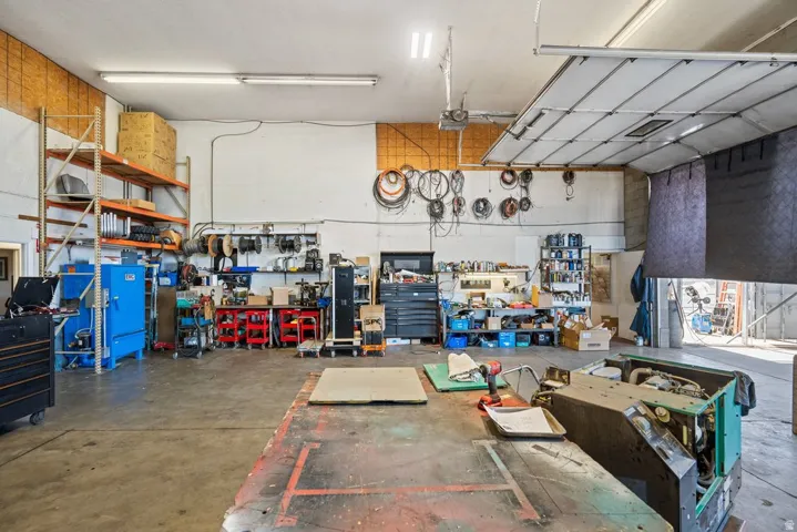 Spacious commercial workshop featuring a concrete floor, high ceilings with fluorescent lighting, industrial shelving, a large overhead door, and ample wall storage
