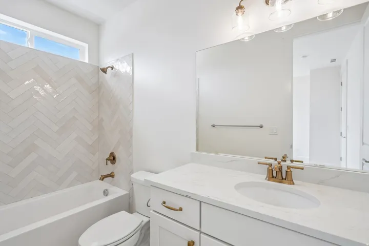Bathroom featuring a tub/shower combination with white herringbone tile surround, a white vanity with a light-colored countertop, and a large wall-mounted mirror