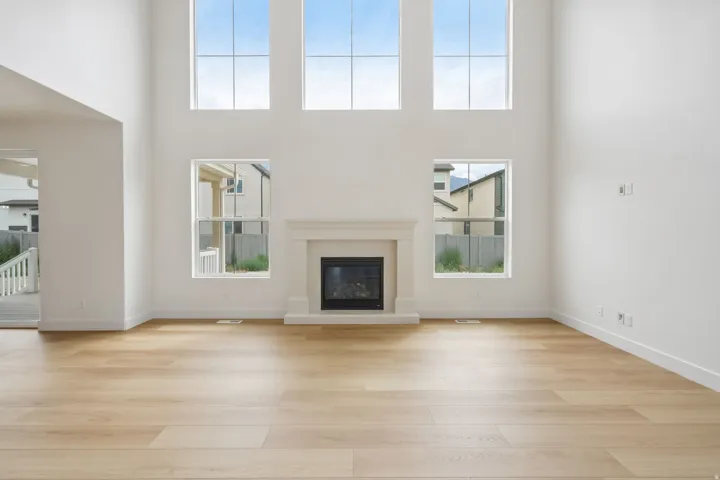 Living area featuring a fireplace with a mantel, soaring ceilings, wood-finish flooring, and multiple large windows