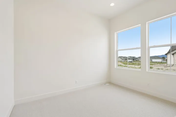 Bright interior room featuring two large windows, recessed ceiling lighting, light-toned carpeting, and white baseboards