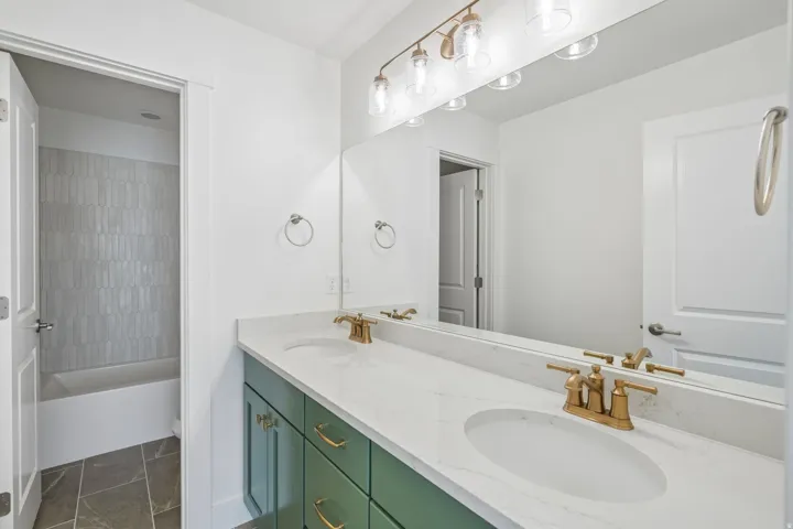 Bathroom vanity featuring dual undermount sinks with brass fixtures, a white stone-finish countertop, and green cabinetry
