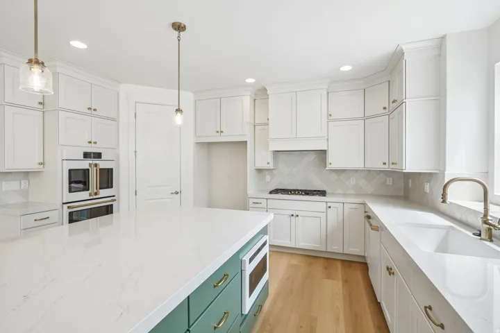 Kitchen featuring a large island with a built-in microwave, white shaker-style cabinetry, light wood-finish flooring, a patterned tile backsplash, and a double wall oven