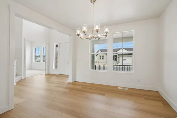 Light wood-finish flooring throughout, featuring a multi-light chandelier and multiple windows