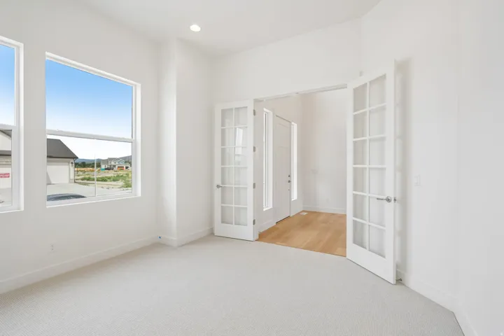 Spacious room with light-toned carpet, ample natural light from multiple large windows, and a pair of French doors