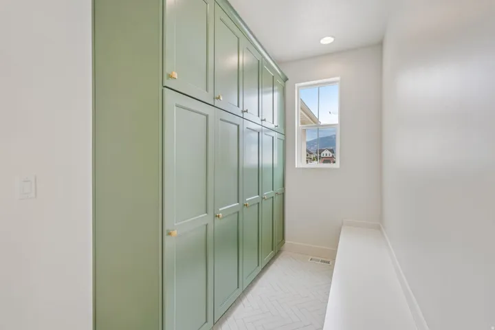 Floor-to-ceiling sage green cabinetry with gold hardware, recessed lighting, and a window providing natural illumination