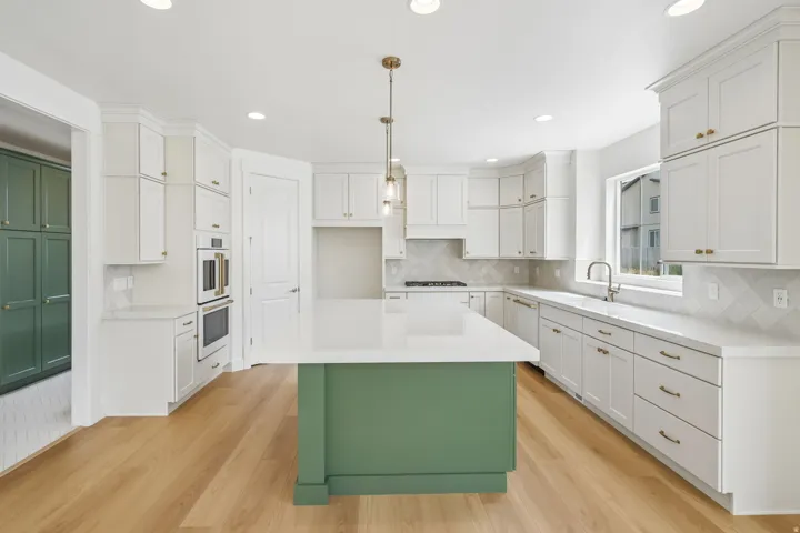 Kitchen featuring a central island with a green base and white countertop, white perimeter cabinetry with brass hardware, wood-finish flooring, and integrated stainless steel double ovens