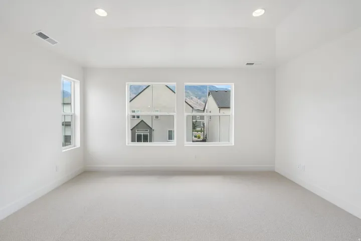 Spacious room featuring neutral carpet flooring, crisp white walls, multiple windows, recessed lighting, and a tray ceiling