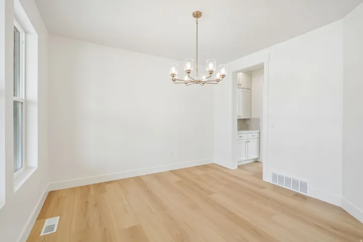 Light-filled room featuring wood-finish flooring, a contemporary six-light chandelier with clear glass shades, white walls, and white trim