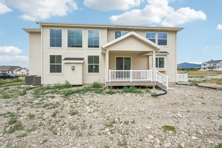 Rear exterior showcasing a covered patio with white railing, a sliding glass door, and multiple large windows on both levels