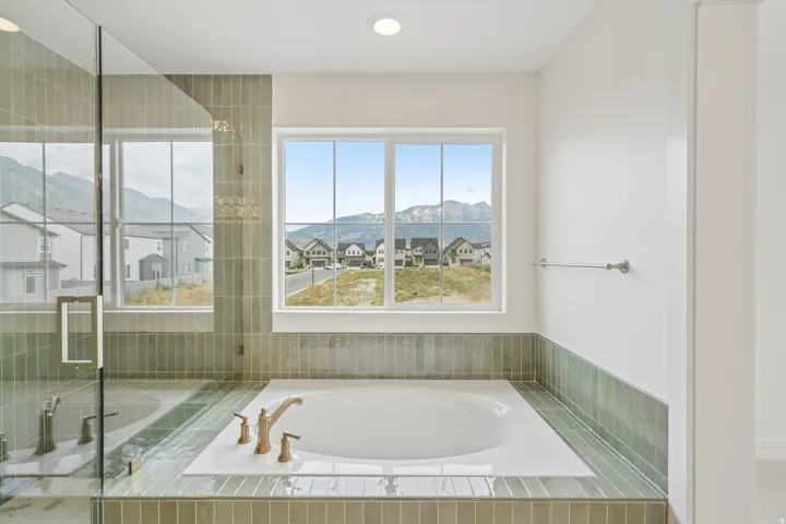 Built-in soaking tub with bronze-finish fixtures, surrounded by green vertical subway tile