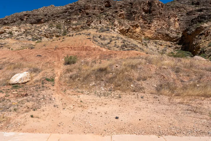 Natural desert landscape featuring a rocky hillside and scattered brush