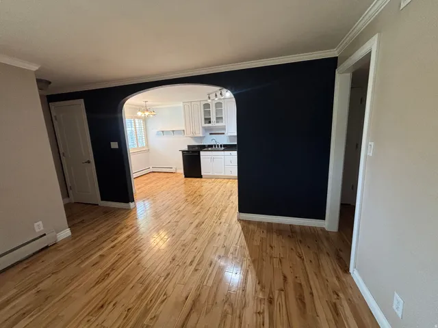 Hardwood flooring extending into an arched entryway, showcasing a kitchen with white cabinetry, black appliances, and a window with plantation shutters