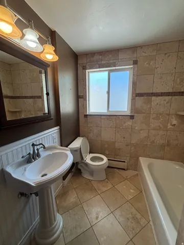 Full bathroom featuring floor-to-ceiling tile, pedestal sink with a chrome faucet, and a window with frosted lower pane