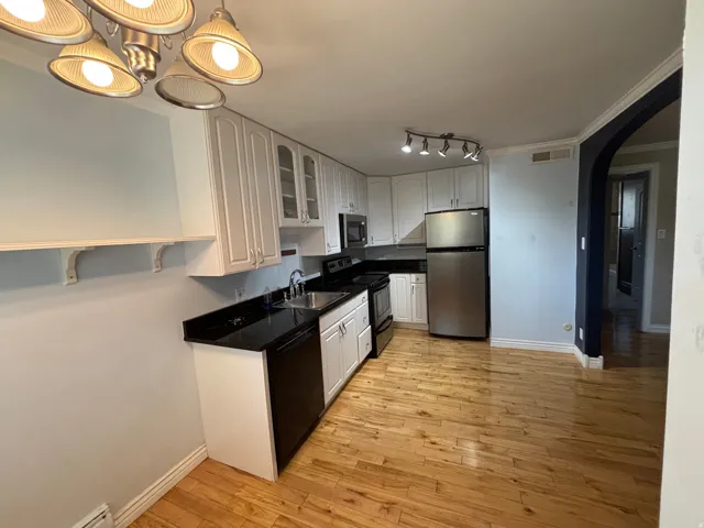 Kitchen featuring wood-finish flooring, white cabinetry, dark countertops, and stainless steel appliances
