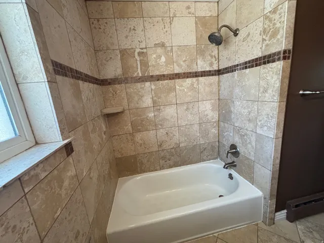 Bathtub and shower combination with stone tile surround and decorative tile accent band