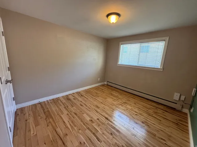 Spacious room featuring wood-finish flooring, neutral-toned walls, and a window with blinds