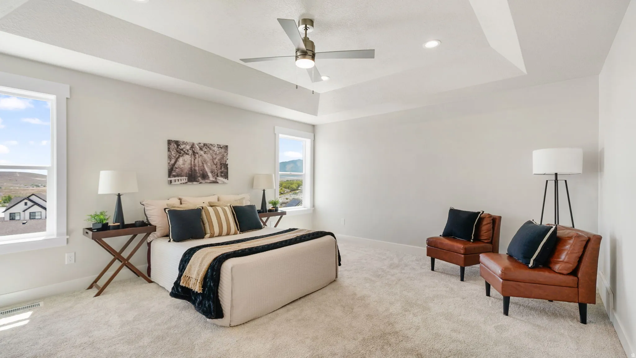 Spacious bedroom featuring light-toned carpeting, a tray ceiling with recessed lighting and a ceiling fan, and multiple large windows