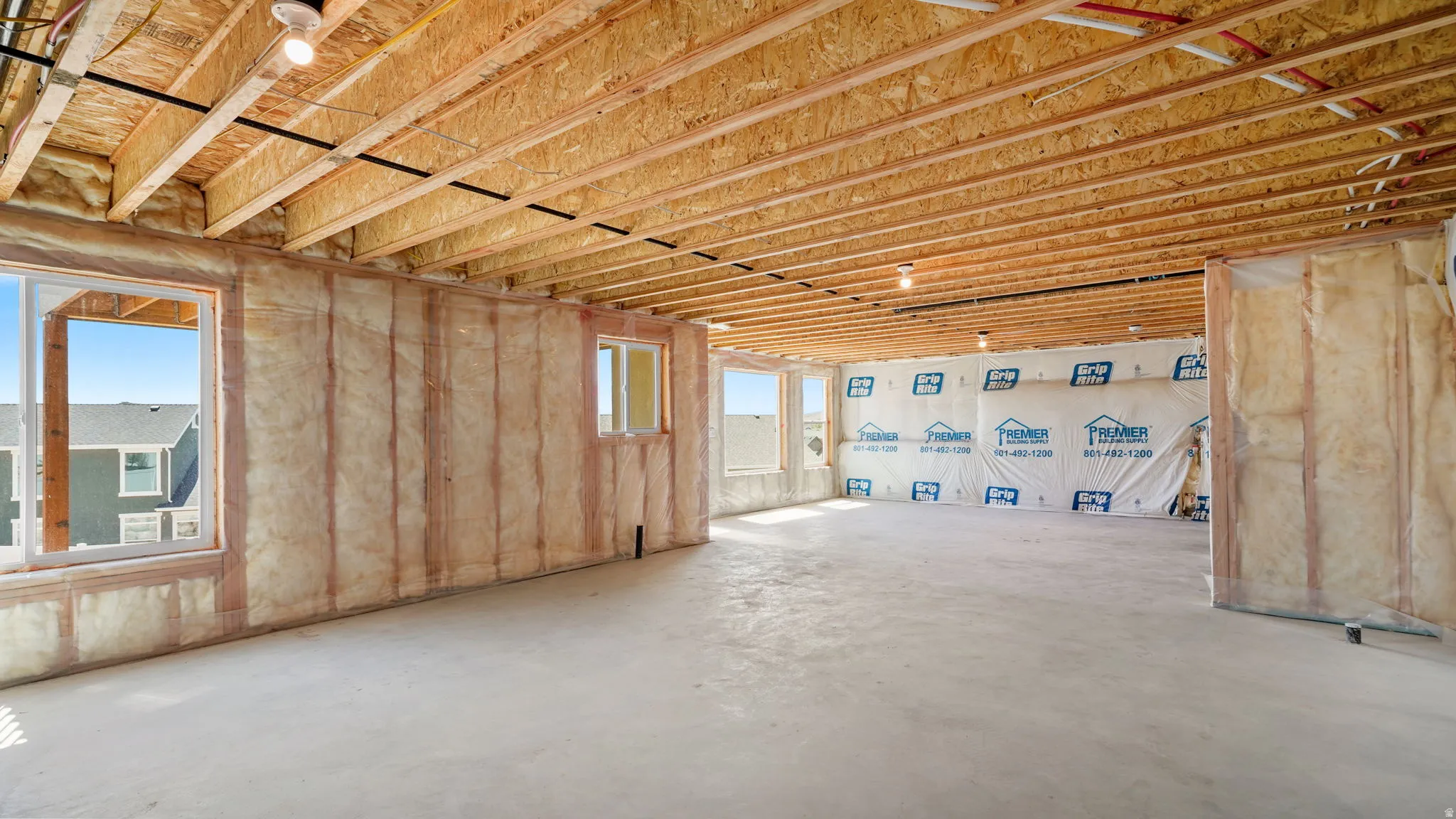 Unfinished basement space featuring exposed wood joists and subfloor, multiple windows, batt insulation, and a concrete floor