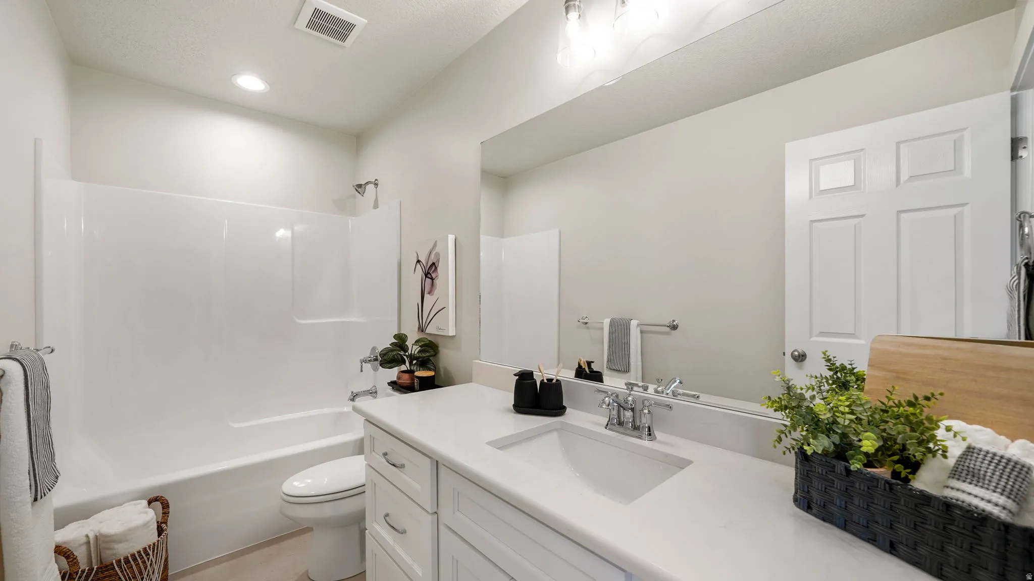 Bright bathroom featuring a white vanity with an integrated sink, polished chrome faucet, and expansive mirror