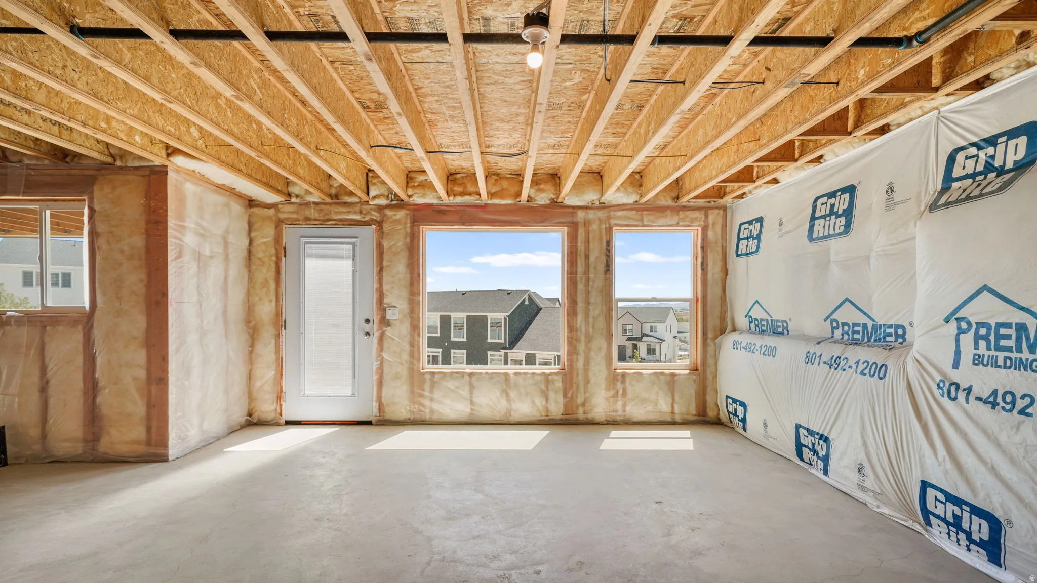 Unfinished lower level featuring an egress door, three windows, exposed ceiling joists, and concrete flooring
