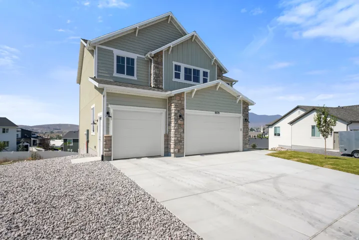 Contemporary exterior with light green siding and stone accents, featuring two attached garages and a concrete driveway