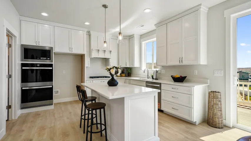 Modern kitchen featuring white shaker cabinetry, stainless steel appliances including a built-in microwave and double ovens, light wood-finish flooring, and a center island with countertop seating