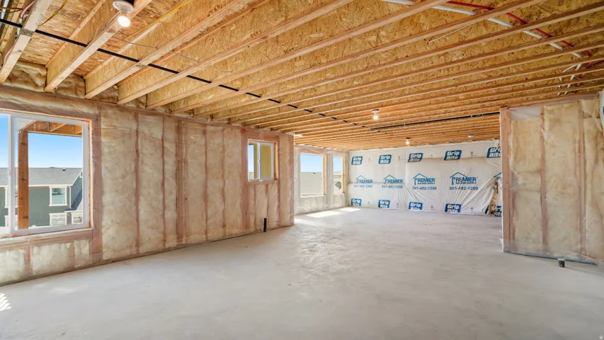 Unfinished basement space featuring exposed wood joists and subfloor, multiple windows, batt insulation, and a concrete floor